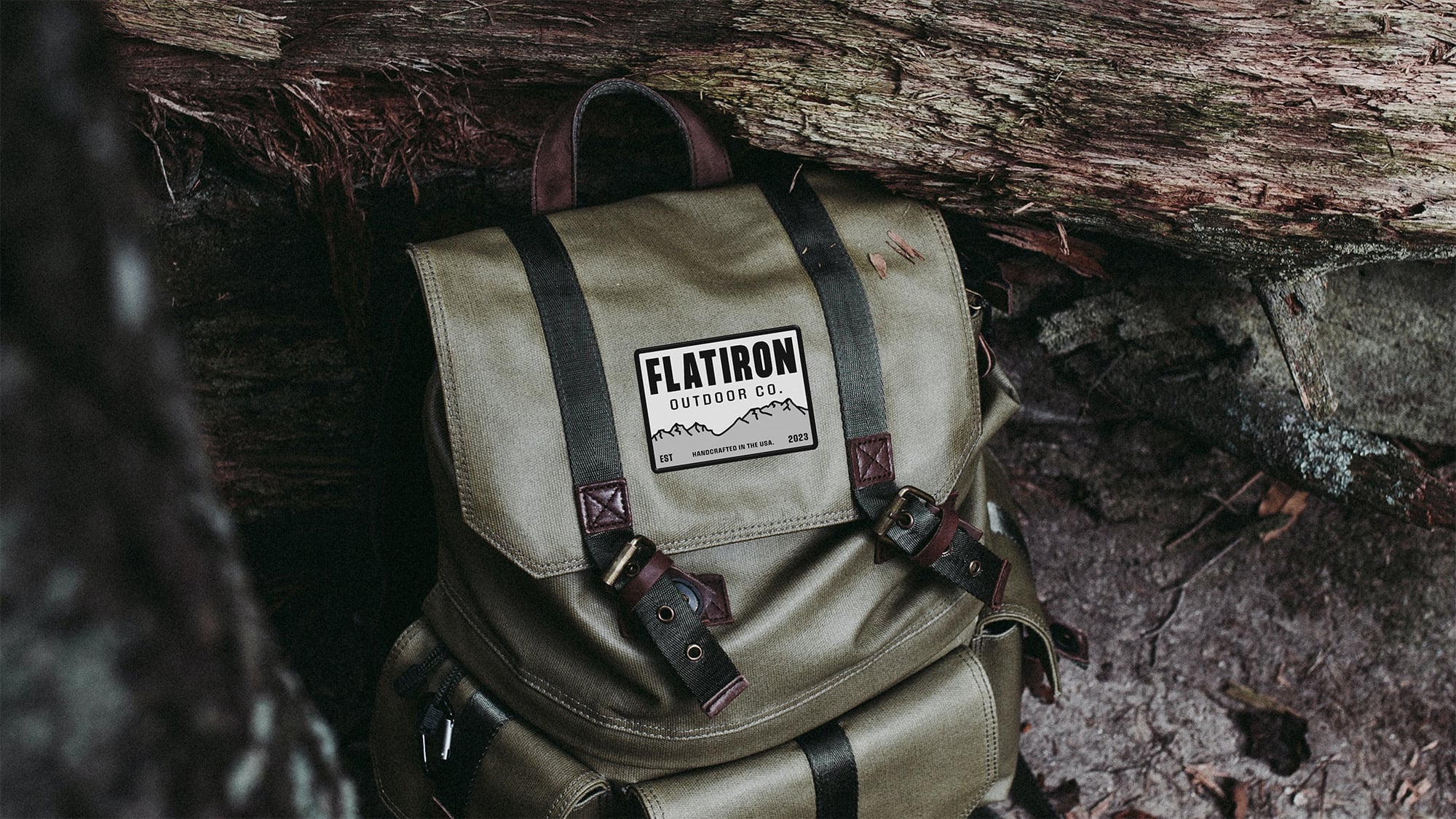 A rugged olive green outdoor backpack with leather accents, featuring the Flatiron Outdoor Co. mountain logo patch.