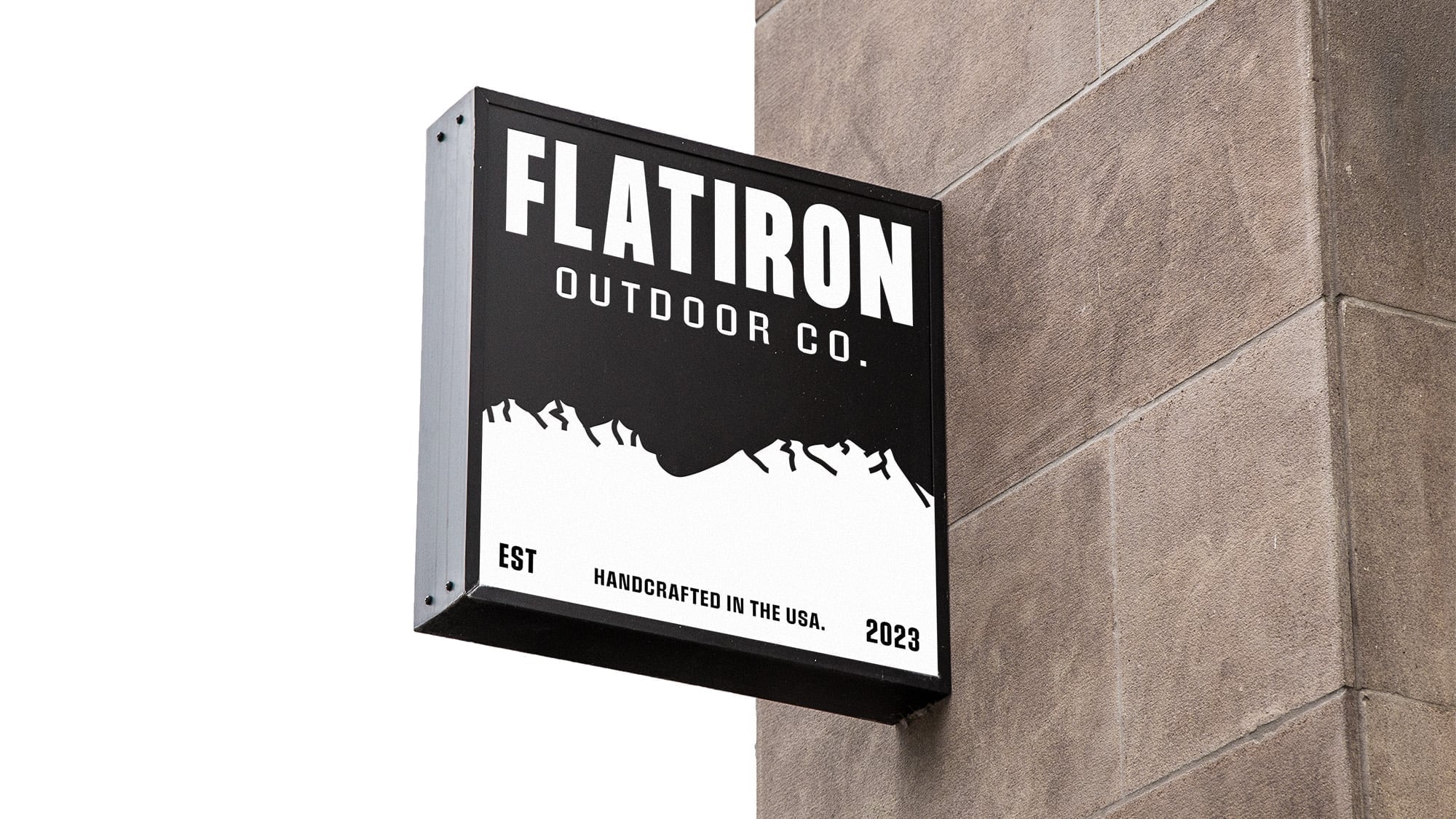 A modern black outdoor storefront sign featuring the white Flatiron Outdoor Co. mountain logo on a stone building.