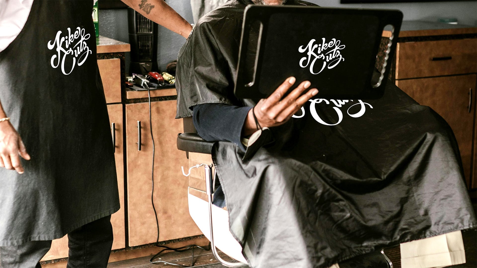 A professional barber wearing a branded Kike Cutz apron in a high-end salon setting.